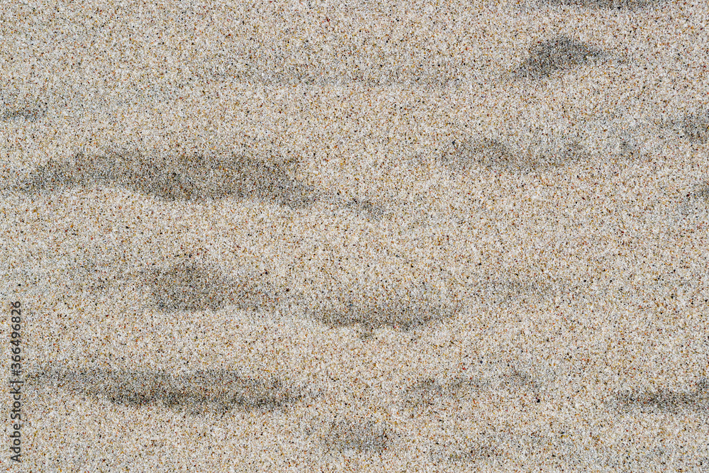 Sandy, grainy, granular surface of orange, gray, white, beige, and brown grains of sand with wavy spots of dark, wet sand, closeup shot on beach of sea coast. Natural mineral background for design. Sandy, grainy, granular surface of orange, gray, white, beige, and brown grains of sand with wavy spots of dark, wet sand, closeup shot on beach of sea coast. Natural mineral background for design.