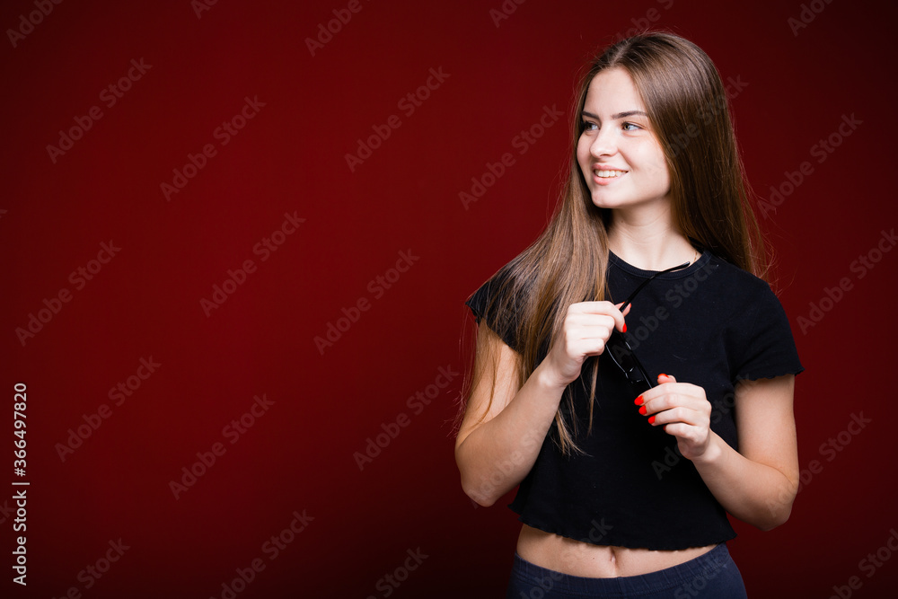 Portrait of a girl with long hair who dances in a black T-shirt on a red background and looks to the side Portrait of a girl with long hair who dances in a black T-shirt on a red background and looks to the side