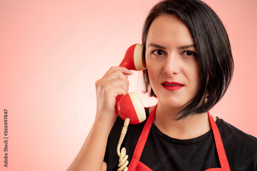 Woman employed at supermarket with red apron and black t-shirt talking on an old recever Woman employed at supermarket with red apron and black t-shirt talking on an old recever