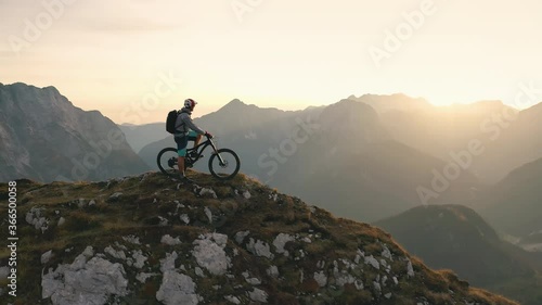 Aerial - Flyover shot of a mountain biker standing on top of the mountain at sunset. 4K