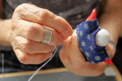 つるし飾りの人形を作るシニアの女性の手。