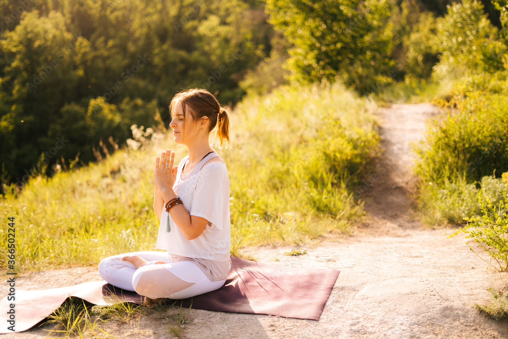 Relaxed young woman is meditating in lotus position with closed eyes sitting on yoga mat. Female yoga instructor doing namaste pose. Lady enjoying meditation. Girl prayer meditating in Namaste mudra. Relaxed young woman is meditating in lotus position with closed eyes sitting on yoga mat. Female yoga instructor doing namaste pose. Lady enjoying meditation. Girl prayer meditating in Namaste mudra.