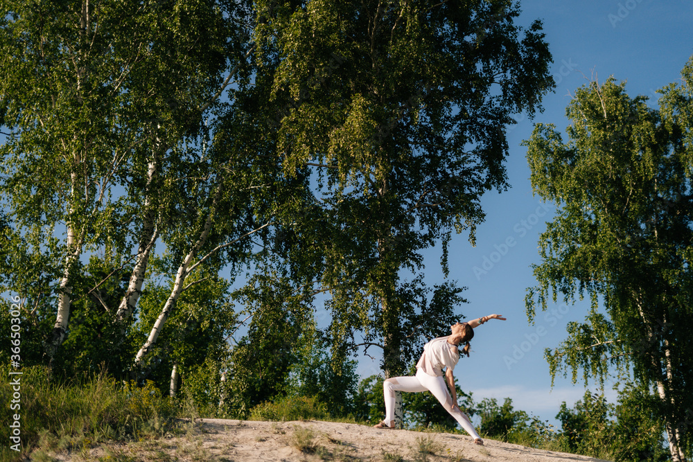 Sporty young woman doing yoga Warrior Pose on clear sunny day at nature. Pretty yoga instructor is performing Virabhadrasana pose outside. Sporty young woman doing yoga Warrior Pose on clear sunny day at nature. Pretty yoga instructor is performing Virabhadrasana pose outside.