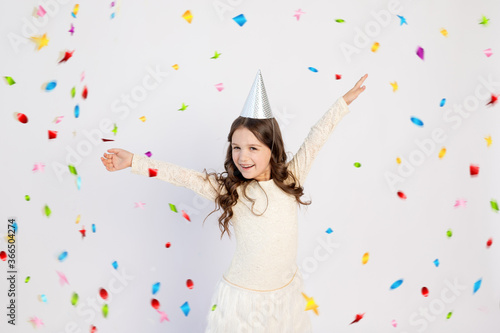 A cute little girl with a cap on a white isolated background with a serpentine dancing and rejoicing. Space for text. Little girl celebrates birthday, holiday concept