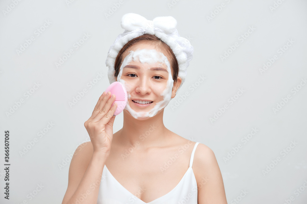 Happy young Asian woman applying foaming cleanser on her face and wearing towel on her head. Happy young Asian woman applying foaming cleanser on her face and wearing towel on her head.