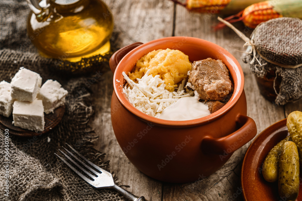 Delicious polenta with meat, cheese and sour cream in bowl on rustic wooden background. Traditional Romanian food, close up Delicious polenta with meat, cheese and sour cream in bowl on rustic wooden background. Traditional Romanian food, close up