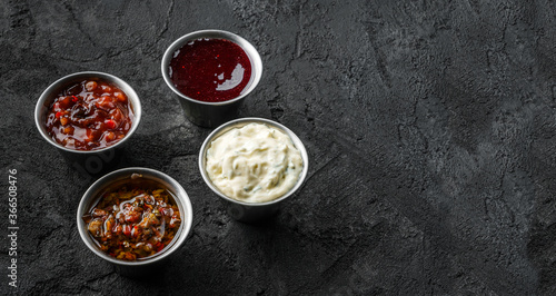 Set of different sauces, mayonnaise, hot pepper, tomato garlic sauce, berry spicy sauce in bowl on black stone background