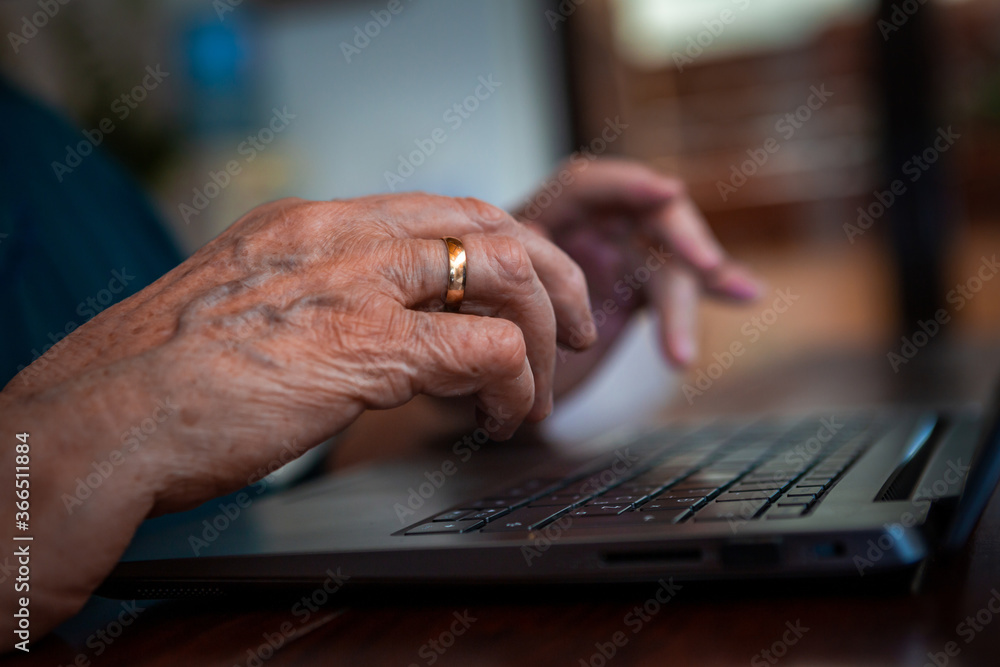 Focus on the hand of an elderly senior lady using a laptop. She searches for something on the internet. On his hand is an old engagement gold ring.