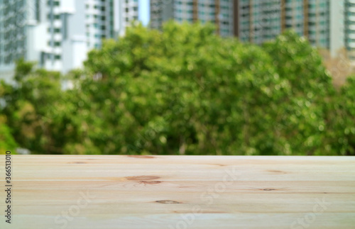 Empty wooden table at the balcony with blurry green foliage and modern building in background