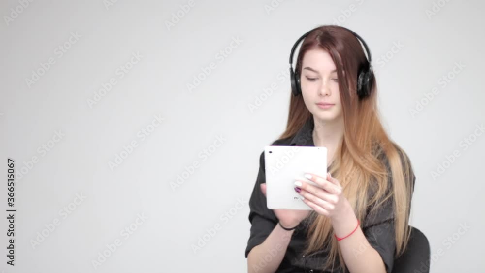 Young good looking woman with long hair using white tablet to listen to music in black wireless headphones Young good looking woman with long hair using white tablet to listen to music in black wireless headphones