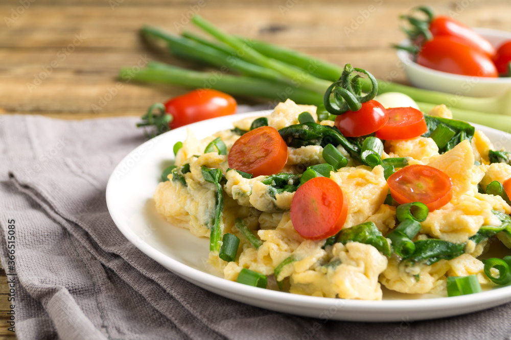 scrambled eggs with spinach and tomatoes on a white plate. scrambled eggs with spinach and tomatoes on a white plate.