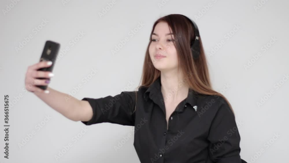 Young good looking girl with long hair posing in wireless headphones taking a selfie photograph with smartphone Young good looking girl with long hair posing in wireless headphones taking a selfie photograph with smartphone