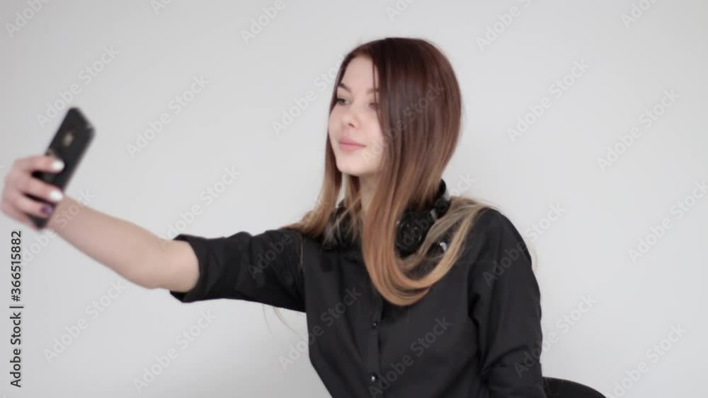 Good looking young girl with long hair taking black wireless headphones off her head and posing for a selfie photograph