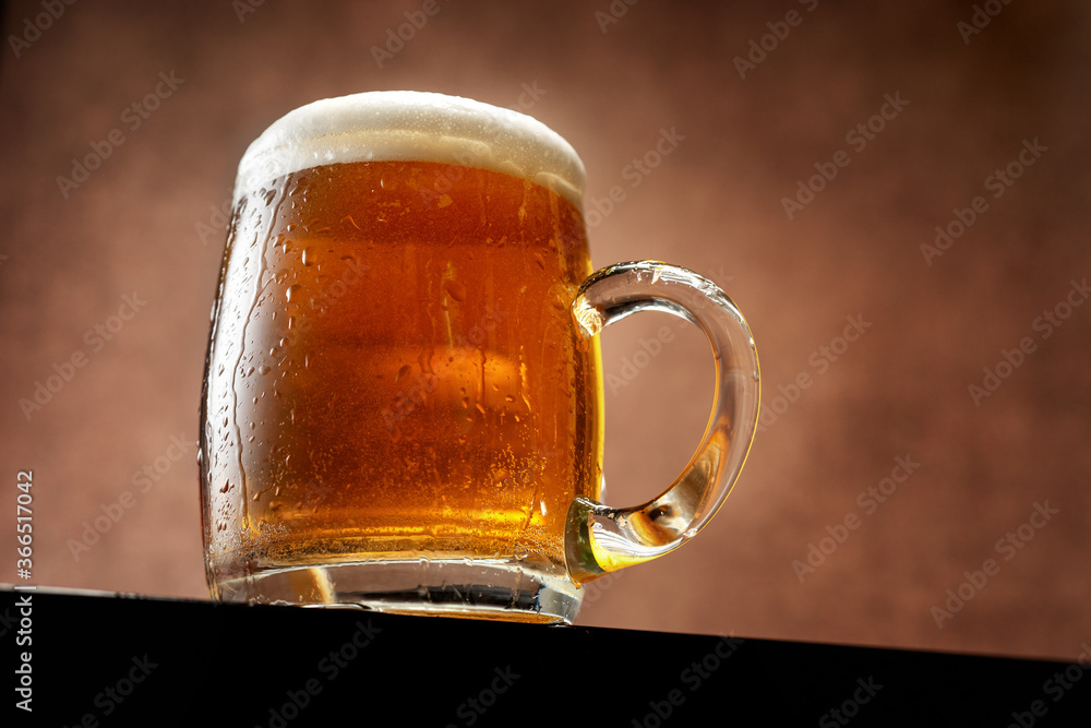 Mug of beer with foam standing against brown background