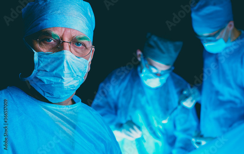 Group of surgeons at work in operating theater toned in blue. Medical team performing operation