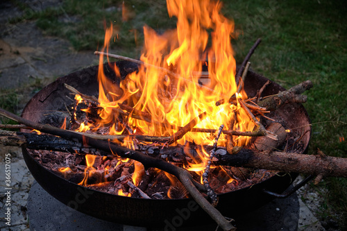 A natural bonfire with wooden sticks and branches is burning in a fire bowl at night. Seen in Germany in July.