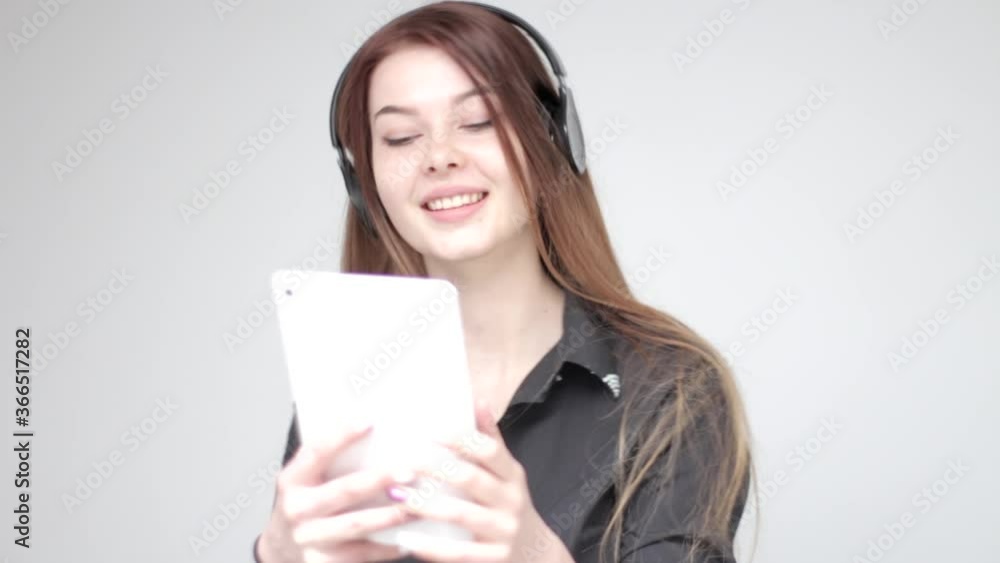 Good looking young woman with long hair in headphones smiling listening to music and taking a selfie photo with white tablet Good looking young woman with long hair in headphones smiling listening to music and taking a selfie photo with white tablet