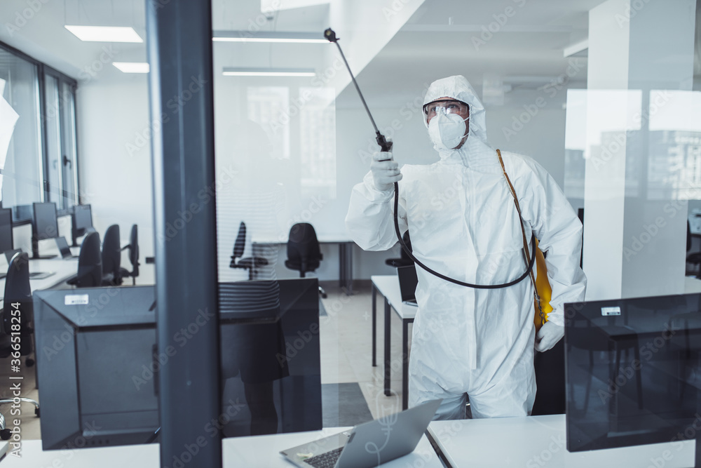 Office disinfection during COVID-19 pandemic. Man in protective suit and face mask spraying for disinfection in the office Office disinfection during COVID-19 pandemic. Man in protective suit and face mask spraying for disinfection in the office
