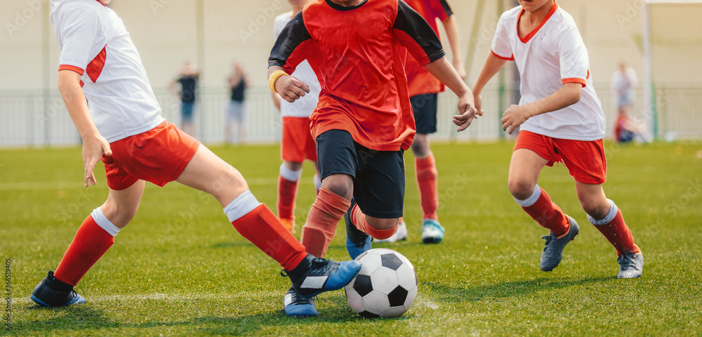 Multi-ethnic children playing soccer game. Young boys running after soccer ball on grass football field. Kids in red and white jersey shirts Multi-ethnic children playing soccer game. Young boys running after soccer ball on grass football field. Kids in red and white jersey shirts