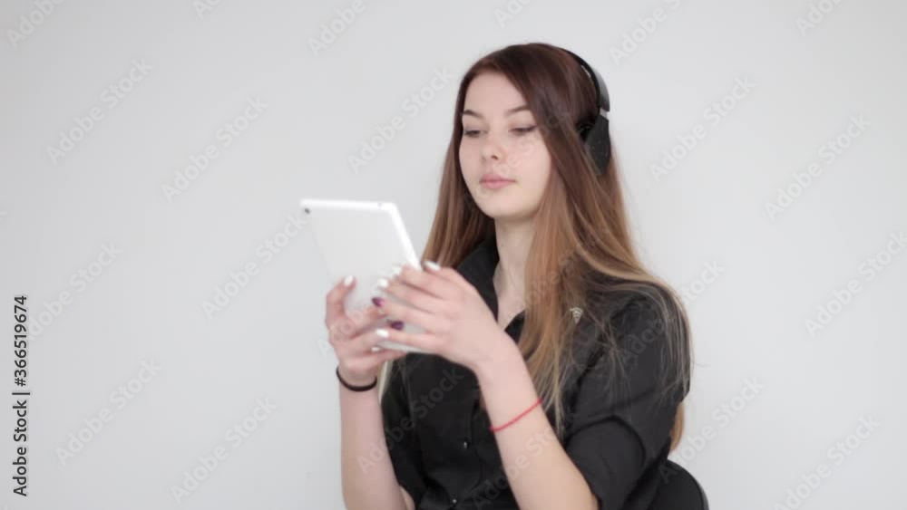 Happy young pretty woman with long dyed hair listening to musin with wireless black headphones on white tablet Happy young pretty woman with long dyed hair listening to musin with wireless black headphones on white tablet