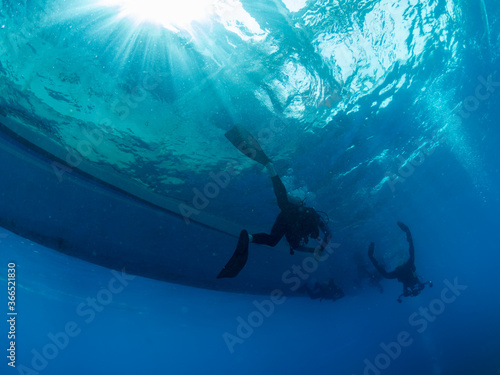 Divers approaching the boat under the water. Clear blue waters and beams of sun, Philippines