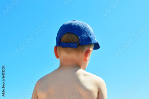 close-up - the back of a boy without a T-shirt on a hot day against a blue sky, a blue cap on his head