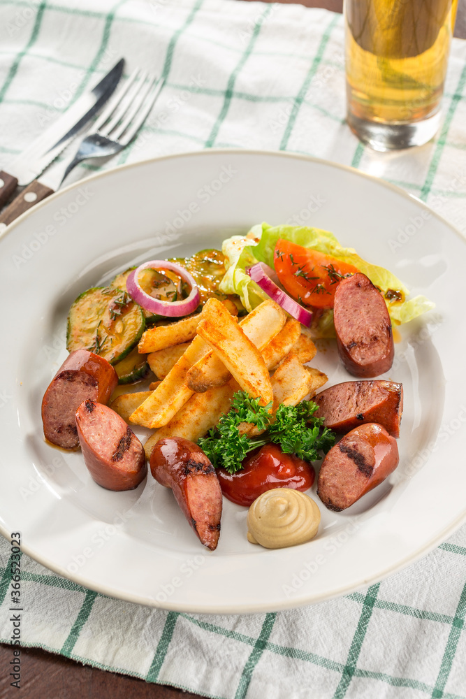 grilled sliced sausage served with beer, french fries, zucchini and ketchup on the side for Octoberfest on the table