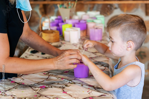 Adorable kid with craftsperson trimming candle wicks on homemade candles