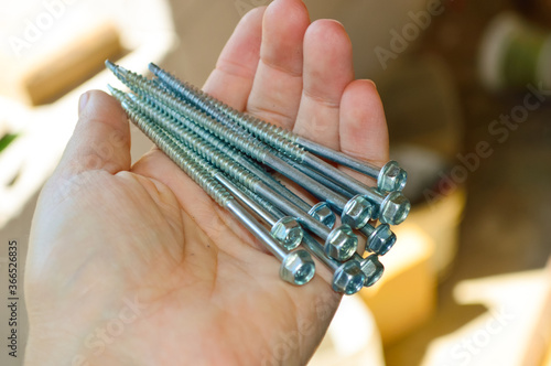 close-up - long screws in a female hand against the background of the construction of a house