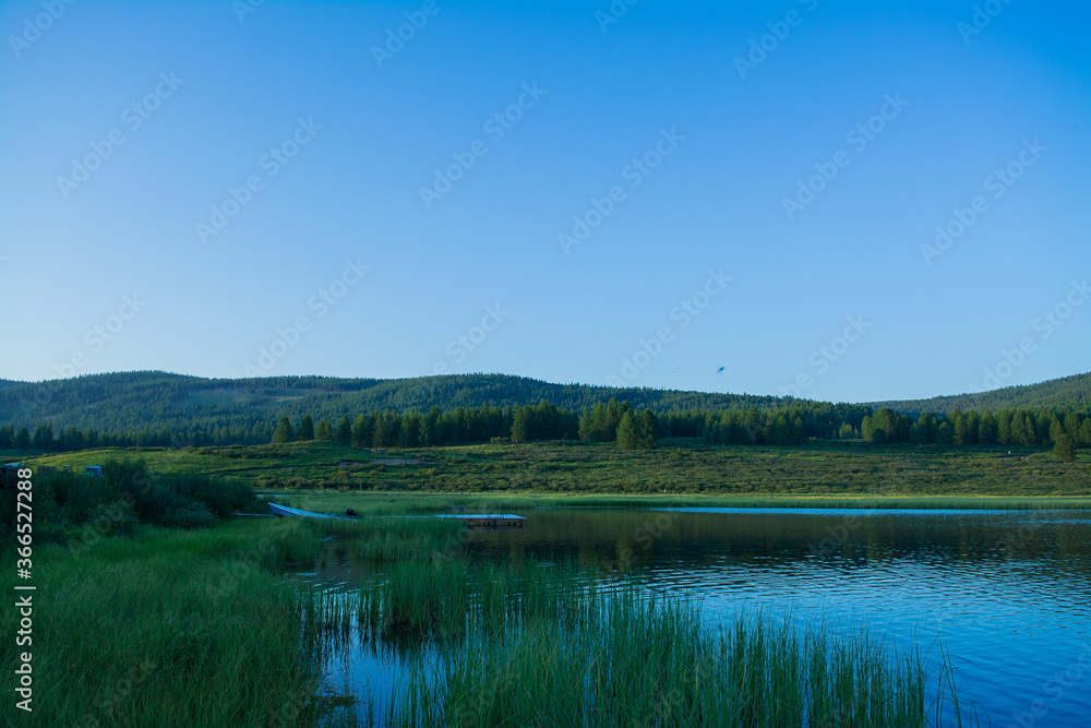 A beautiful mountain lake with reeds surrounded by mountain ranges and impenetrable forests. The lake is high in the Altai mountains