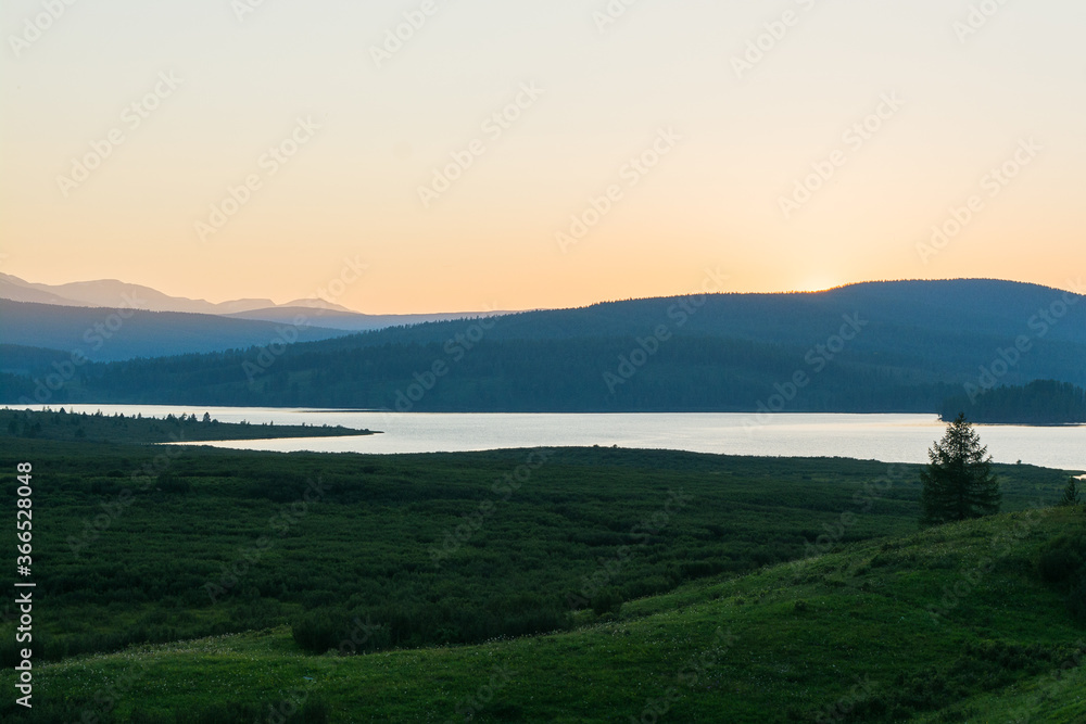 Sunset in the valley of a mountain lake. A beautiful mountain lake with reeds surrounded by mountain ranges and impenetrable forests. The lake is high in the Altai mountains.