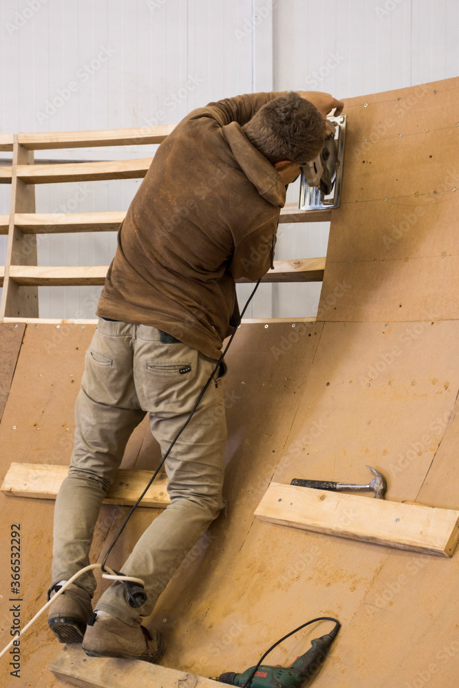 Man working on a wooden indoor skatepark Man working on a wooden indoor skatepark