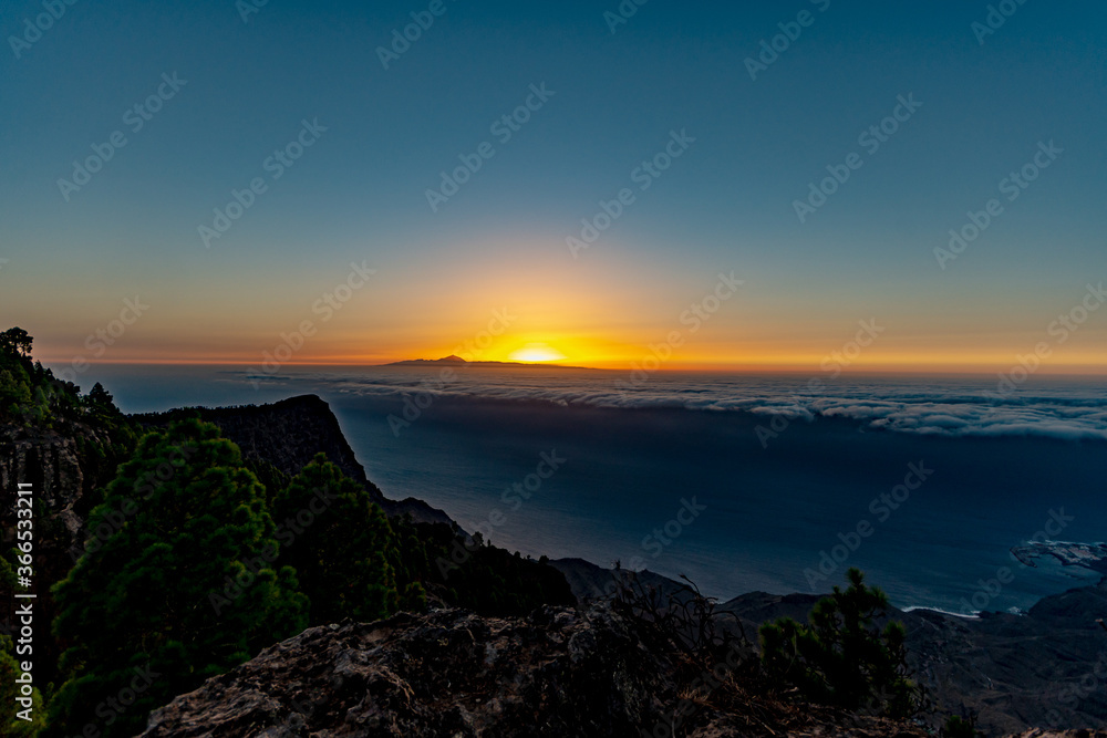 sunset from the canaries, the island of gran canaria with the roque faneque and the teide in the background bathed by a sea of clouds and the reflections and lux of the sun, in tamadaba natural park.