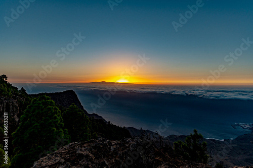 sunset from the canaries, the island of gran canaria with the roque faneque and the teide in the background bathed by a sea of clouds and the reflections and lux of the sun, in tamadaba natural park. © Ral