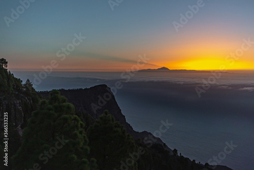 sunset from the canaries, the island of gran canaria with the roque faneque and the teide in the background bathed by a sea of clouds and the reflections and lux of the sun, in tamadaba natural park.