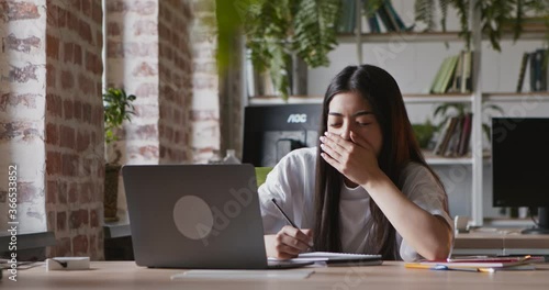 Asian student girl yawning, falling asleep while watching webinar on laptop