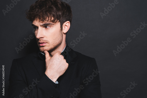 handsome man in formal wear touching face and looking away on black