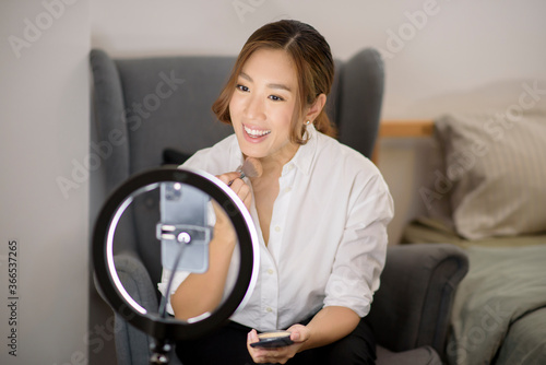 Fototapeta Naklejka Na Ścianę i Meble -  A beautiful Asian makeup blogger is live streaming how to beauty face makeup in her home, beauty and technology concept