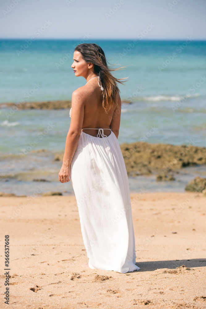 Woman in white dress and back to the air standing on the beach