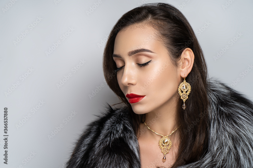 Beautiful girl puts on a gorgeous fur coat made of expensive silver fox fur. Luxury jewellery decorates her neck, exclusive necklace made of gem stones. Perfect horizontal banner for new clothes store Beautiful girl puts on a gorgeous fur coat made of expensive silver fox fur. Luxury jewellery decorates her neck, exclusive necklace made of gem stones. Perfect horizontal banner for new clothes store