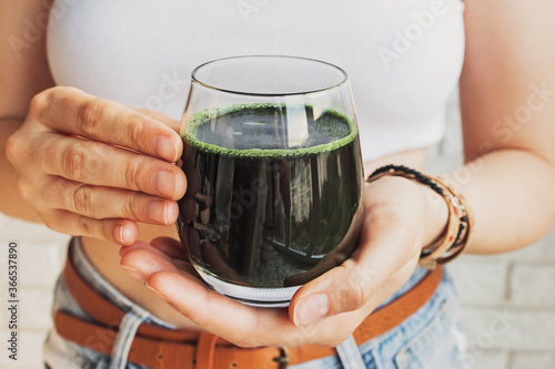 Woman holding glass with healthy spirulina drink close-up photo