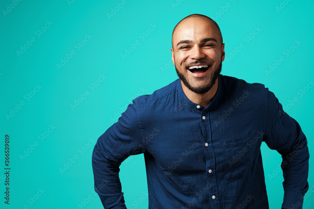Joyful dark-skinned man laughing against turquoise background