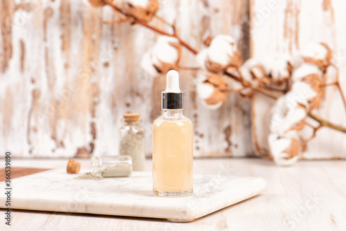 Mockup of moisturizing essence in a dropper glass bottle on a marble tray and wooden table. Cosmetic or spa skincare concept  cotton branch