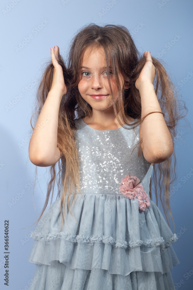 Naklejka premium A beautiful long-haired girl with her favorite items in her hands on a light background in a gray dress with sequins. Foreground. Quarantine, games at home.