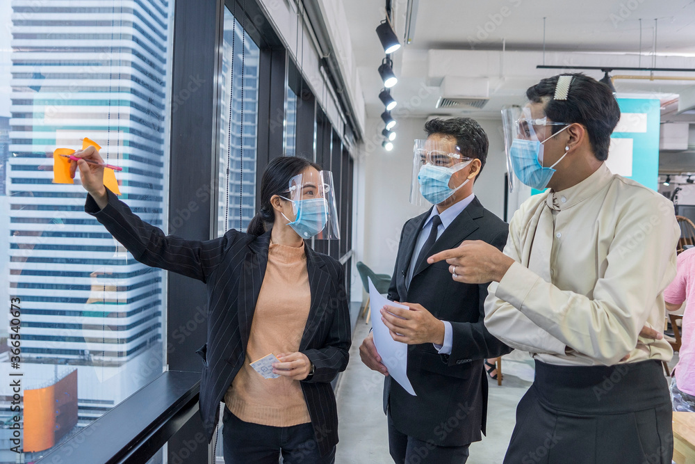 Group of advertising company employees wear masks and face shield and creative brainstorming together for a consultation meeting at office .New normal concept. Group of advertising company employees wear masks and face shield and creative brainstorming together for a consultation meeting at office .New normal concept.