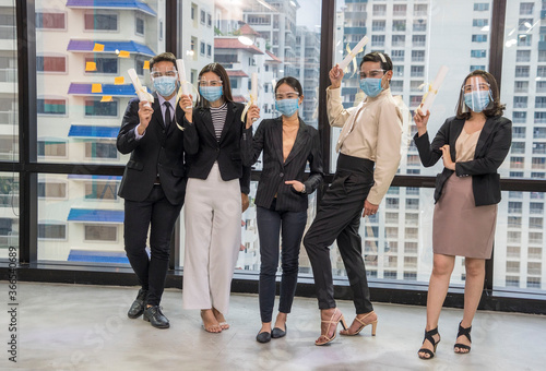 Group of company employees and executives put on a mask, standing in their arms, believing in the team to be successful.Health ,new normal and teamwork concept