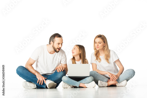 parents sitting on floor near happy daughter with laptop isolated on white