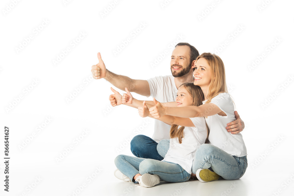 happy family sitting on floor with crossed legs and showing thumbs up isolated on white