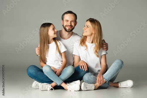 happy family sitting on floor with crossed legs and embracing on grey background