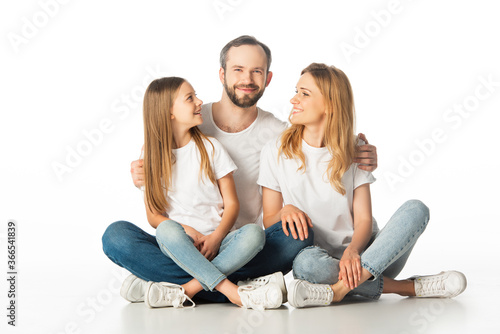 happy family sitting on floor with crossed legs and embracing isolated on white